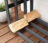 A close-up shot of a log rack on a wooden deck, with a split log resting on it. A potted plant is visible in the background. Podgląd zdjęcia produktu