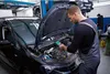 A mechanic is inspecting a car engine with a diagnostic tool in a workshop. Podgląd zdjęcia produktu