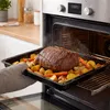 A roasting pan with a cooked roast and vegetables is being removed from an oven. Produktbild-Vorschau