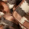 A close-up view of a fluffy blanket with a plaid pattern in shades of brown, white, and gray. The edge of the blanket is visible with a brown trim. Produktbild-Vorschau
