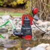 A submersible pump is submerged in shallow water with a green hose attached, surrounded by rocks and foliage. Produktbild-Vorschau