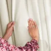 Hands touching a cream-colored curtain. Podgląd zdjęcia produktu