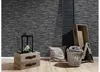 A vignette of home decor items including a lantern on a wooden crate, a pillow, and a basket of towels, set against a stone-effect wallpaper. Náhľad obrázku produktu