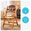 A wooden high chair is shown in a well-lit room with a chair and lamp in the background. Two circular icons are present on the right side of the image. Náhled obrázku produktu