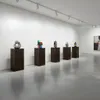 An art gallery setting with several sculptures displayed on dark wooden pedestals. Anteprima dell’immagine prodotto