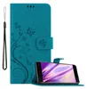 A teal flip phone case with a floral and butterfly design is shown open, with a smartphone inside. A wrist strap is attached to the left side of the case. Náhled obrázku produktu
