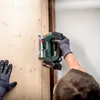 A person wearing work gloves is using a cordless jigsaw to cut into a wooden panel. Podgląd zdjęcia produktu