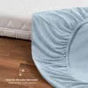 A light blue fitted sheet is shown draped over the corner of a mattress, with a wooden floor in the background. A small graphic indicates suitability for cold weather. Produktbild-Vorschau