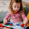 A young girl is sitting on a couch and playing with a soft book. Produktbild-Vorschau