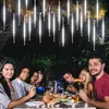 A group of people are having a dinner party outdoors at night, with string lights hanging above. Produktbild-Vorschau