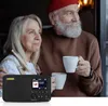 An older couple is looking out a window, holding mugs of coffee. A portable radio is in the foreground. Produktbild-Vorschau
