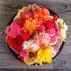 A top-down view of a round arrangement of colorful flowers and leaves in a black pot. Produktbild-Vorschau