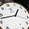 A close-up view of a modern wooden wall clock with a white face and black numbers and hands. Voir les images du produit