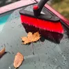 A close-up of a red and black brush with a telescopic handle, resting on a wet car windshield with fallen autumn leaves. Anteprima dell’immagine prodotto