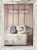 A vintage-style alarm clock and a folded blanket rest on top of a white suitcase, framed by a distressed wooden border. Podgląd zdjęcia produktu
