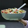 A hand holding a large bowl of pasta salad with cherry tomatoes, mozzarella balls, and basil. Produktbild-Vorschau