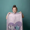 A young girl is holding up a towel with a Lilo and Stitch design. Produktbild-Vorschau