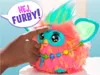 A hand is touching a Furby toy, which has a speech bubble above it. Podgląd zdjęcia produktu