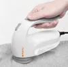 A hand holding a white fabric shaver over a gray piece of fabric. Podgląd zdjęcia produktu