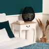 A bedside table with a lamp and books next to a bed. Produktbild-Vorschau