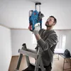 A man is using a cordless hammer drill on the ceiling while standing on a ladder. Produktbild-Vorschau
