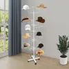 A white metal hat stand with various hats displayed on its multiple tiers, placed indoors near a window with blue curtains. Produktbild-Vorschau
