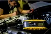 A person is working on a car engine with a battery charger in the foreground. Podgląd zdjęcia produktu
