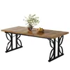 A rectangular dining table with a wooden top and black metal legs, set against a white background. A vase with greenery and a bowl of fruit are placed on the table. Produktbild-Vorschau