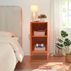 A bedside table with items on and in it, next to a bed and a plant. Podgląd zdjęcia produktu