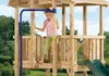 A young girl is playing on a wooden playground structure with a slide. Anteprima dell’immagine prodotto