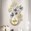 A wall clock with a decorative metal frame shaped like ginkgo leaves, mounted on a wall. Produktbild-Vorschau