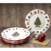 A stack of Christmas-themed plates and one plate displayed on a stand, with decorative ornaments in the foreground. Produktbild-Vorschau