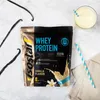 A bag of Isostar Whey Protein powder with vanilla flavor, a glass of prepared drink, and vanilla beans on a marble surface. Produktbild-Vorschau