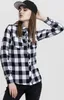 A woman wearing a black baseball cap and a black and white checkered flannel shirt. Náhled obrázku produktu