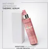 A pink bottle of Kérastase hair serum is leaning against a white geometric block, with text describing the product's benefits. Produktbild-Vorschau