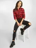 A woman is sitting on a white stool, wearing a red and black checkered shirt and ripped black jeans. Náhled obrázku produktu