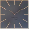 A square wall clock with a dark gray face and wooden hour markers. The clock has rose gold hands and text in the center. Náhled obrázku produktu