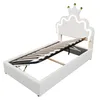 A white upholstered bed frame with a crown-shaped headboard featuring LED lighting and gold accents. The wooden slatted mattress base is lifted to reveal storage space. Produktbild-Vorschau