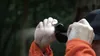 A person is attaching a small black flashlight to the brim of a black baseball cap. Podgląd zdjęcia produktu