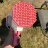 Pink-weiße Blasenpistole, in einer Hand gehalten, von oben gesehen, mit grasbewachsenem Hintergrund Náhled obrázku produktu
