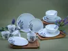 A collection of white porcelain dinnerware with a lavender motif, arranged on wooden trays against a muted green background. Náhľad obrázku produktu