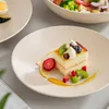A close-up of a slice of cake with fruit on a plate, with other plates and a bowl of salad in the background. Náhled obrázku produktu