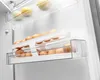 Inside a refrigerator, showing an egg holder with eggs and some fruit on a shelf above. Náhled obrázku produktu
