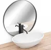 A white oval countertop sink with a black faucet is shown in front of a round mirror. Náhled obrázku produktu