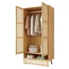 An open, light-colored wooden wardrobe with rattan-style doors, displaying clothes on hangers and storage boxes on shelves. Produktbild-Vorschau