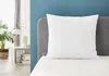 A white pillow is placed on a bed next to a headboard, with a nightstand and plant in the background. Produktbild-Vorschau