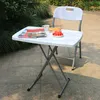 A white folding table with a chair and some items on it, placed outdoors on a stone patio next to some greenery. Produktbild-Vorschau