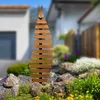 A wooden garden screen is placed in a garden setting with rocks and plants. Produktbild-Vorschau