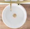 A top-down view of a white round sink with a gold drain and faucet, set against a wooden background. Náhled obrázku produktu
