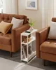 A narrow side table with charging capabilities is placed between two brown leather sofas in a living room setting. Produktbild-Vorschau